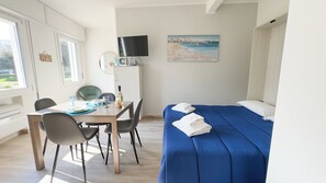 Habitació amb un llit, taula de menjador amb cadires, televisió de pantalla plana i un quadre de paisatge maritim.