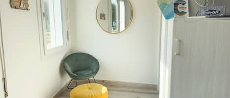 A room with a wooden floor, a green chair, a yellow ottoman, a mirror, and a cabinet with a television.