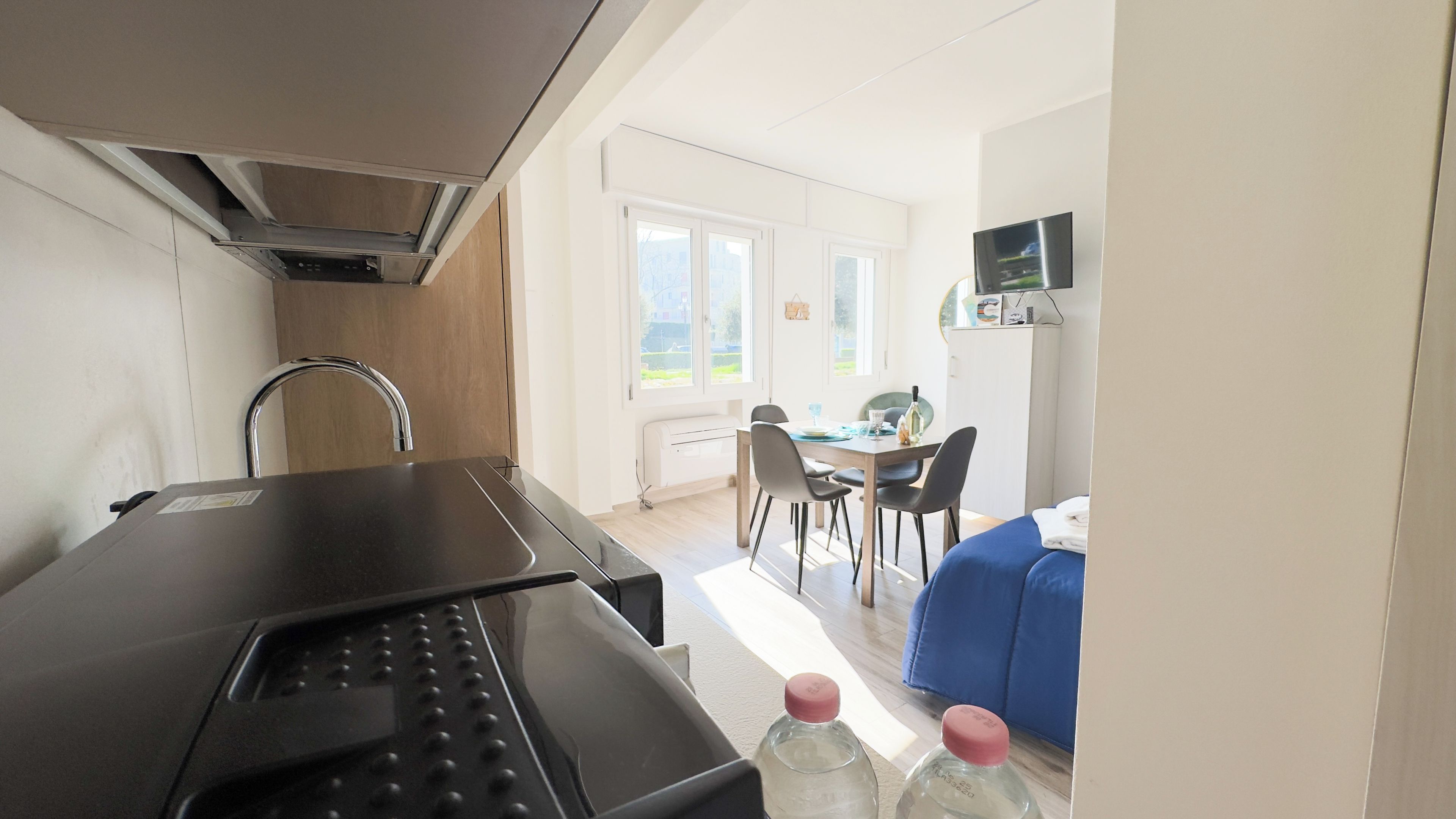 A kitchenette with a modern faucet, a dining area with a table and chairs, and a blue sofa in the background.