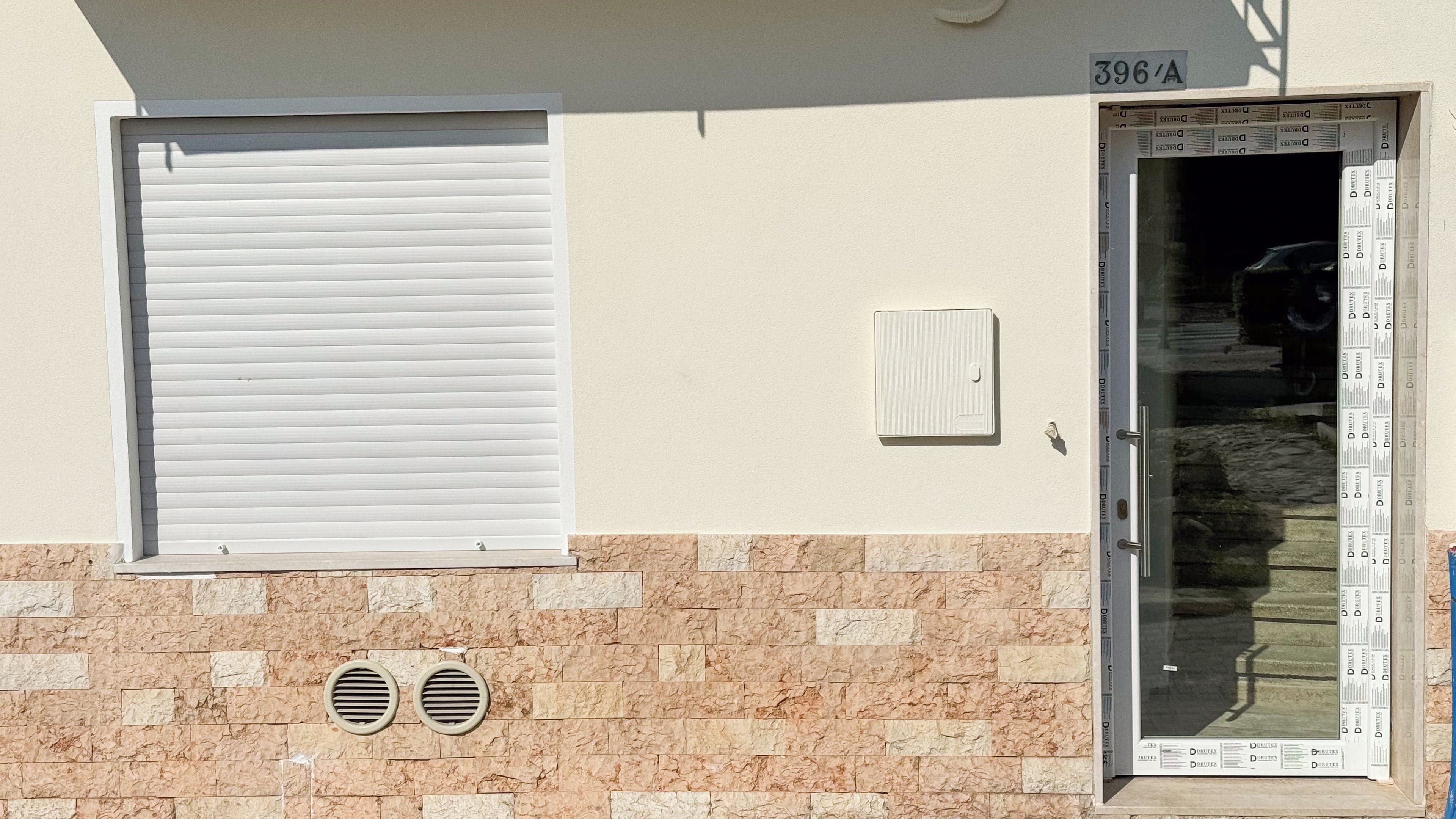 Fachada de um prédio com uma janela fechada, uma porta com jornal e um respiradouro.