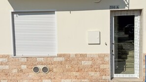 Fachada de edificio con un ventanal cerrado, una puerta con periódicos y una rejilla de ventilación.