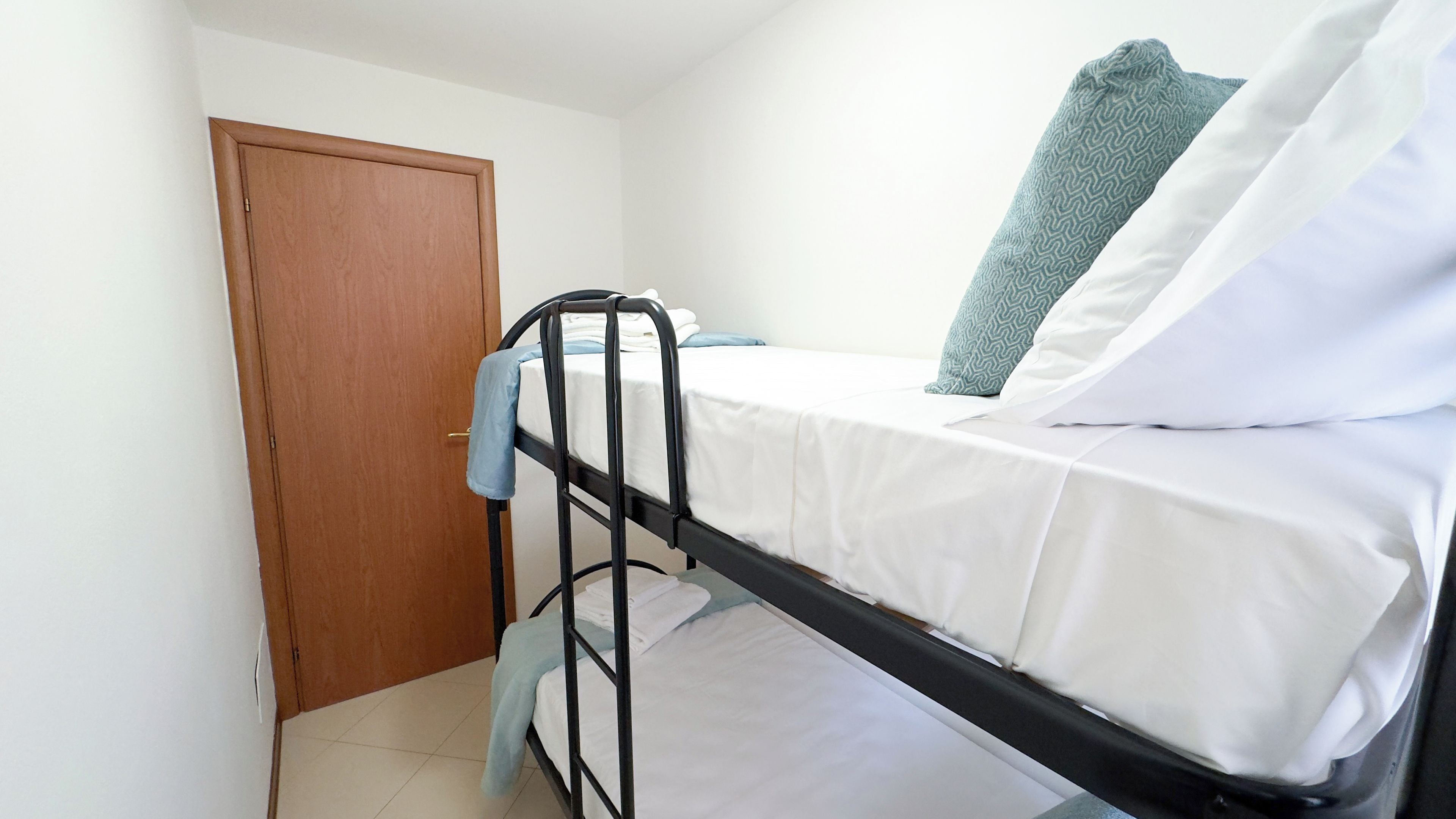 A single bed with a metal frame, white bedding, and a patterned pillow.