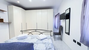 Ein Schlafzimmer mit Bett, Sessel, Kleiderschrank, Fernseher und Spiegel.