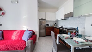 A compact living space with a kitchenette, a dining area, and a red sofa. - Casa Raffi by Ca-sa Check (Chioggia)