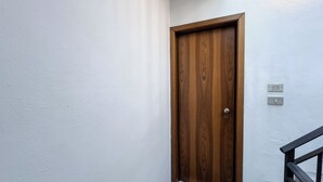 Eine Holztür mit einem Metallgriff, eine weiße Wand und ein schwarzes Geländer.