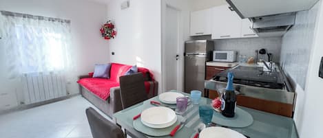 A modern apartment with a dining area, kitchenette, and a living room with a sofa and a decorative wall piece.