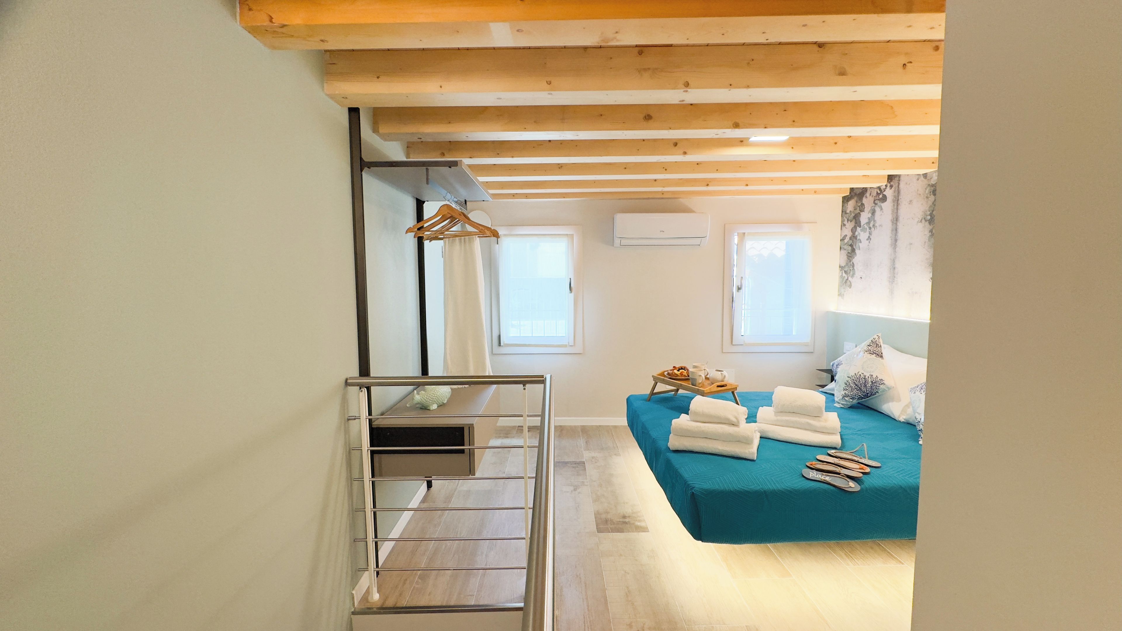 Una habitación con cama, una mesita con toallas y una bandeja, y una ventana con cortinas.