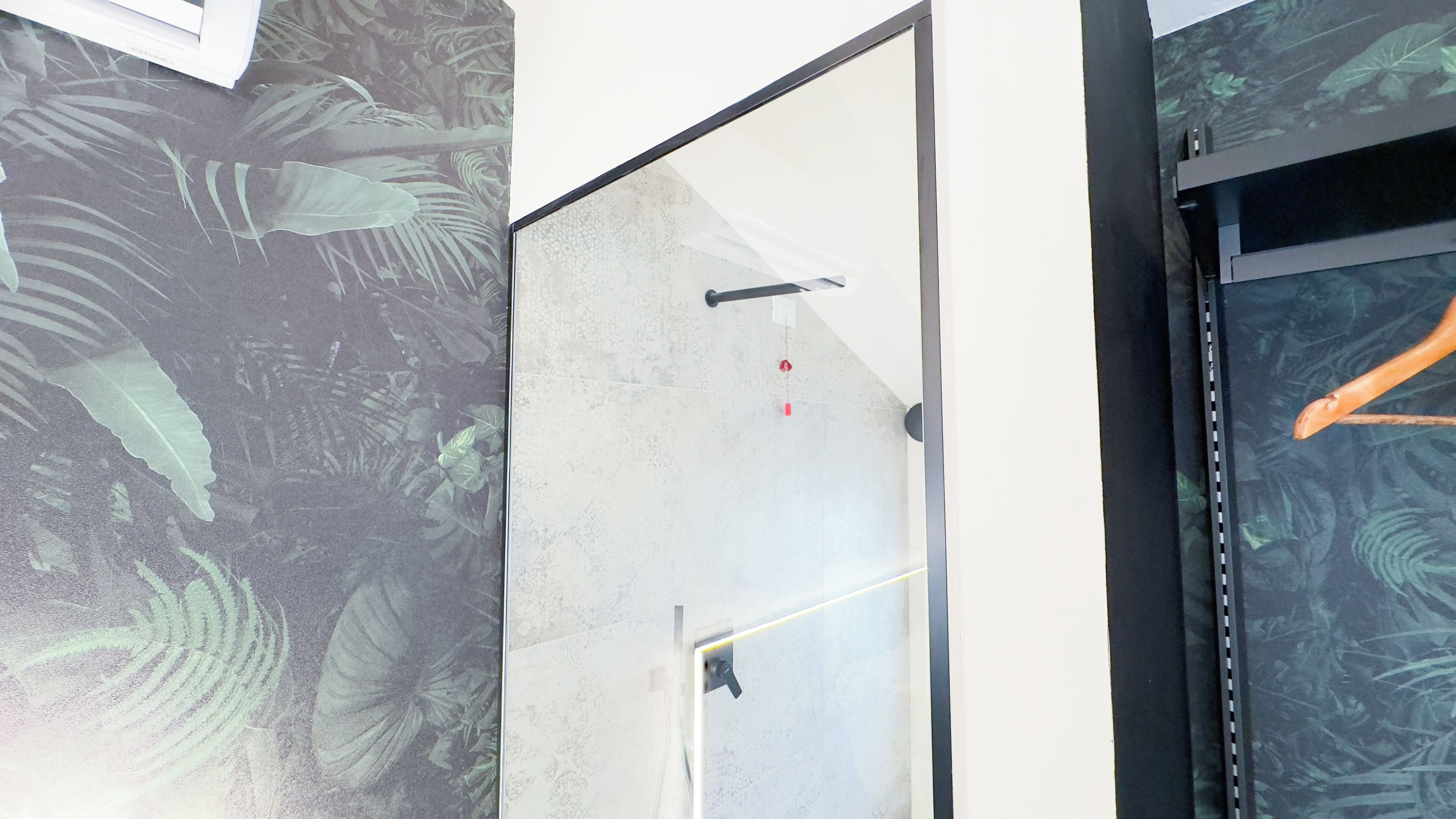 A room with a large window, a door with a handle, and a wall with a leaf pattern.
