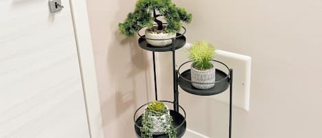 A three-tiered black metal plant stand with potted plants against a wall.