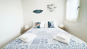 A bed with a patterned bedspread, two pillows with a tropical design, two bedside lamps, and a wall decoration of fish. - Maison la Digue by Ca-sa Check (Chioggia)