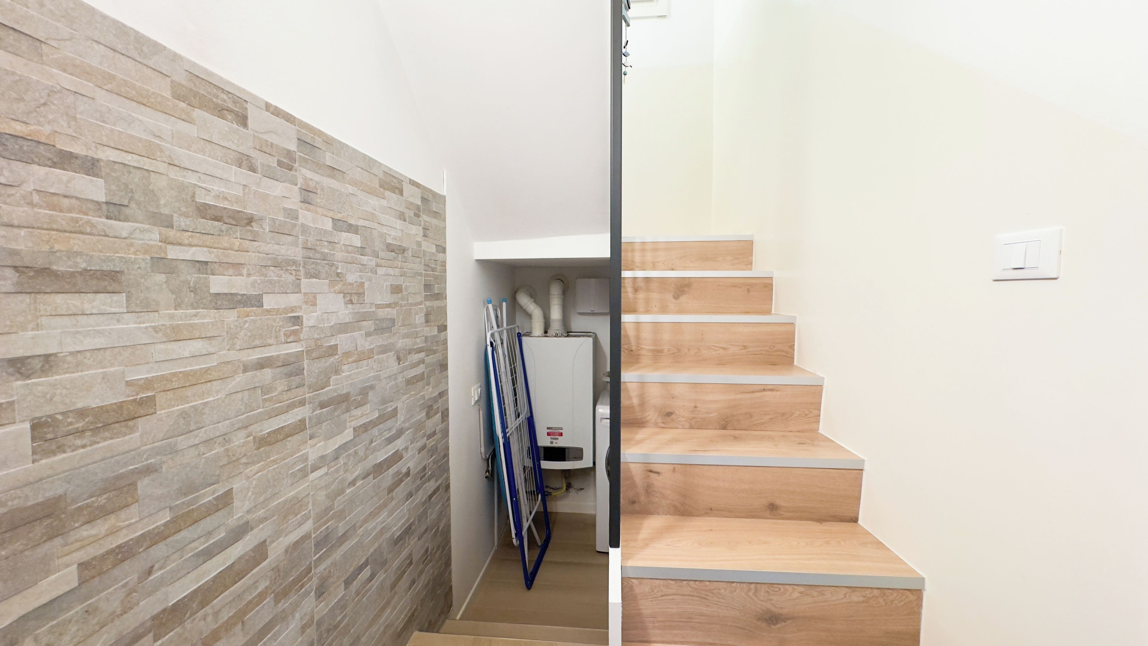 Un pasillo con una pared de piedra a un lado y una escalera de madera al otro.