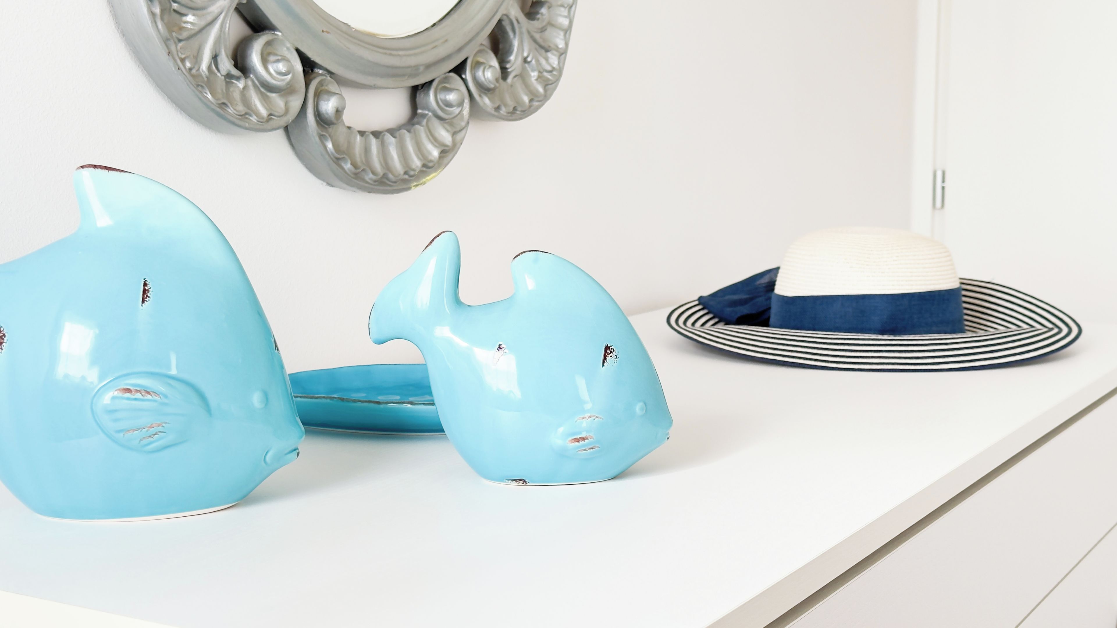 Een wit oppervlak met een decoratieve spiegel, een blauwe keramieken sculptuur en een gestreepte hoed.