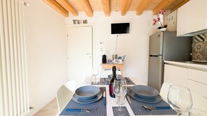 A dining area with a table set for two, a TV mounted on the wall, and a kitchen area with a refrigerator and a microwave. - Maison la Digue by Ca-sa Check (Chioggia)