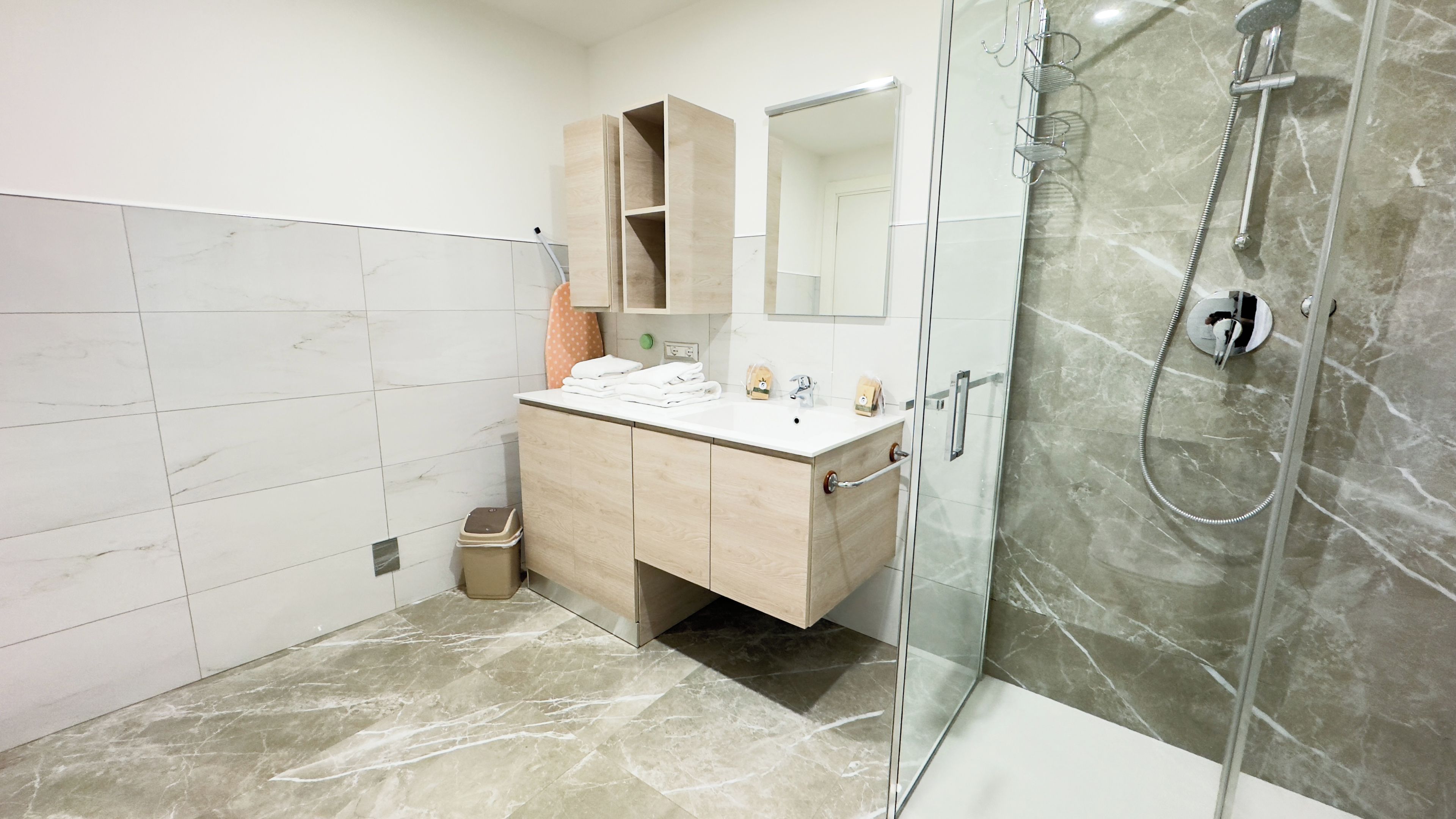 Une salle de bain moderne avec une douche à parois de verre, un meuble-lavabo en bois et un grand miroir.