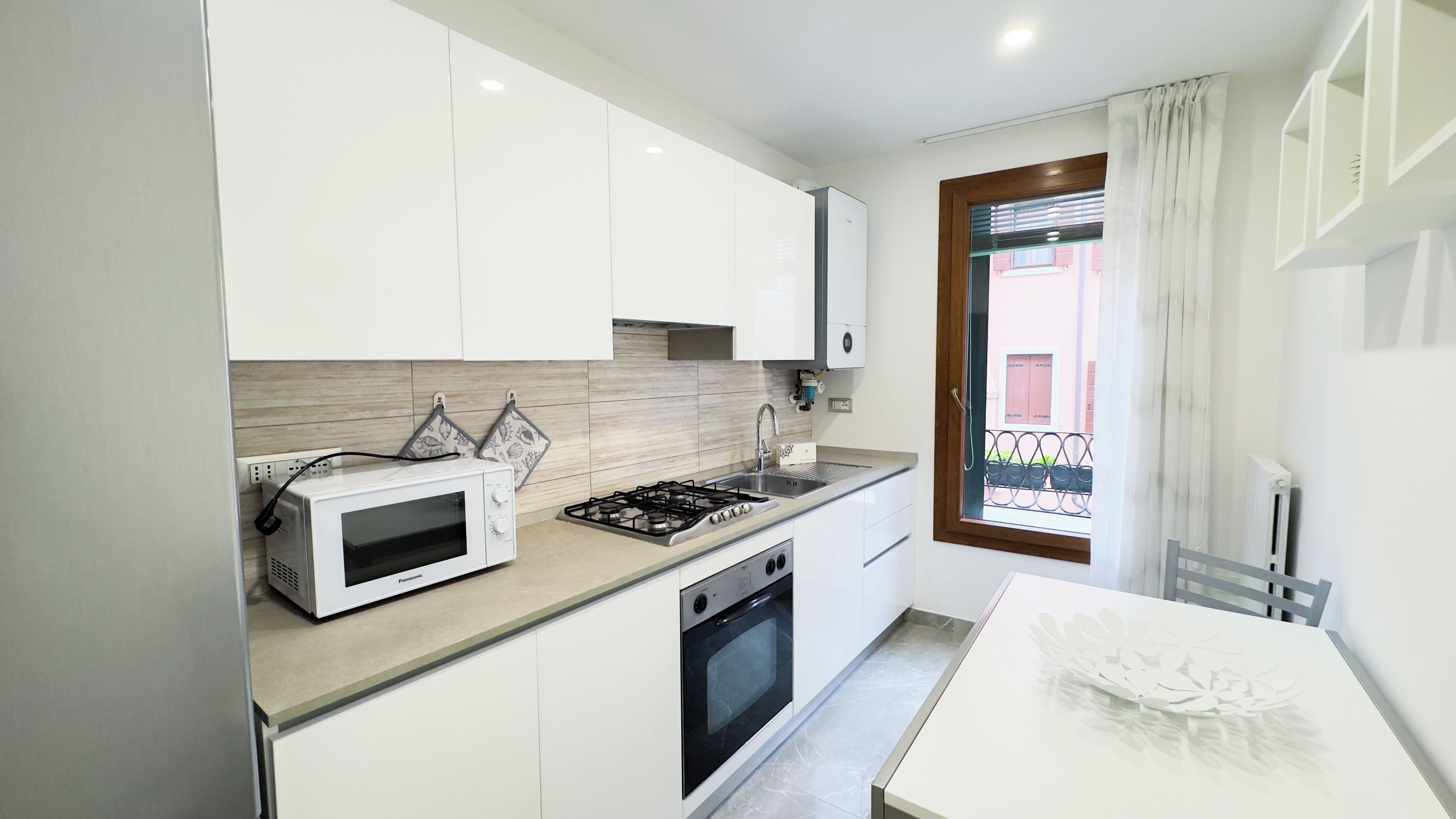 Une cuisine moderne avec des meubles blancs, un four à micro-ondes, une cuisinière à gaz et un four traditionnel.