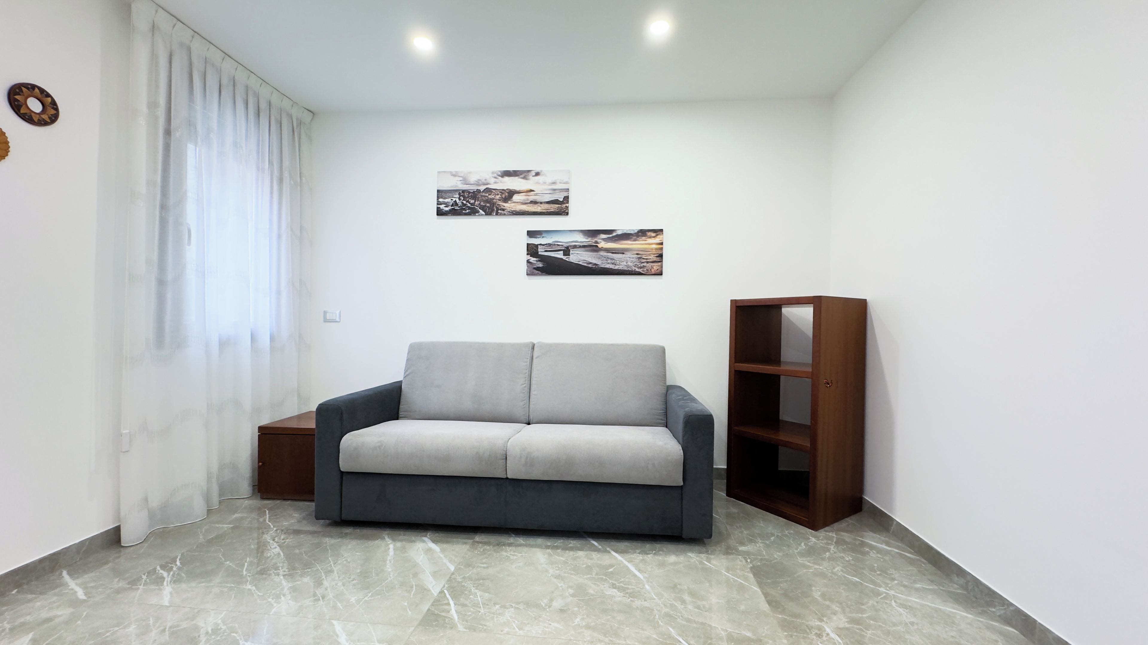 A living room with a grey sofa, a wooden bookshelf, and two wall-mounted pictures.
