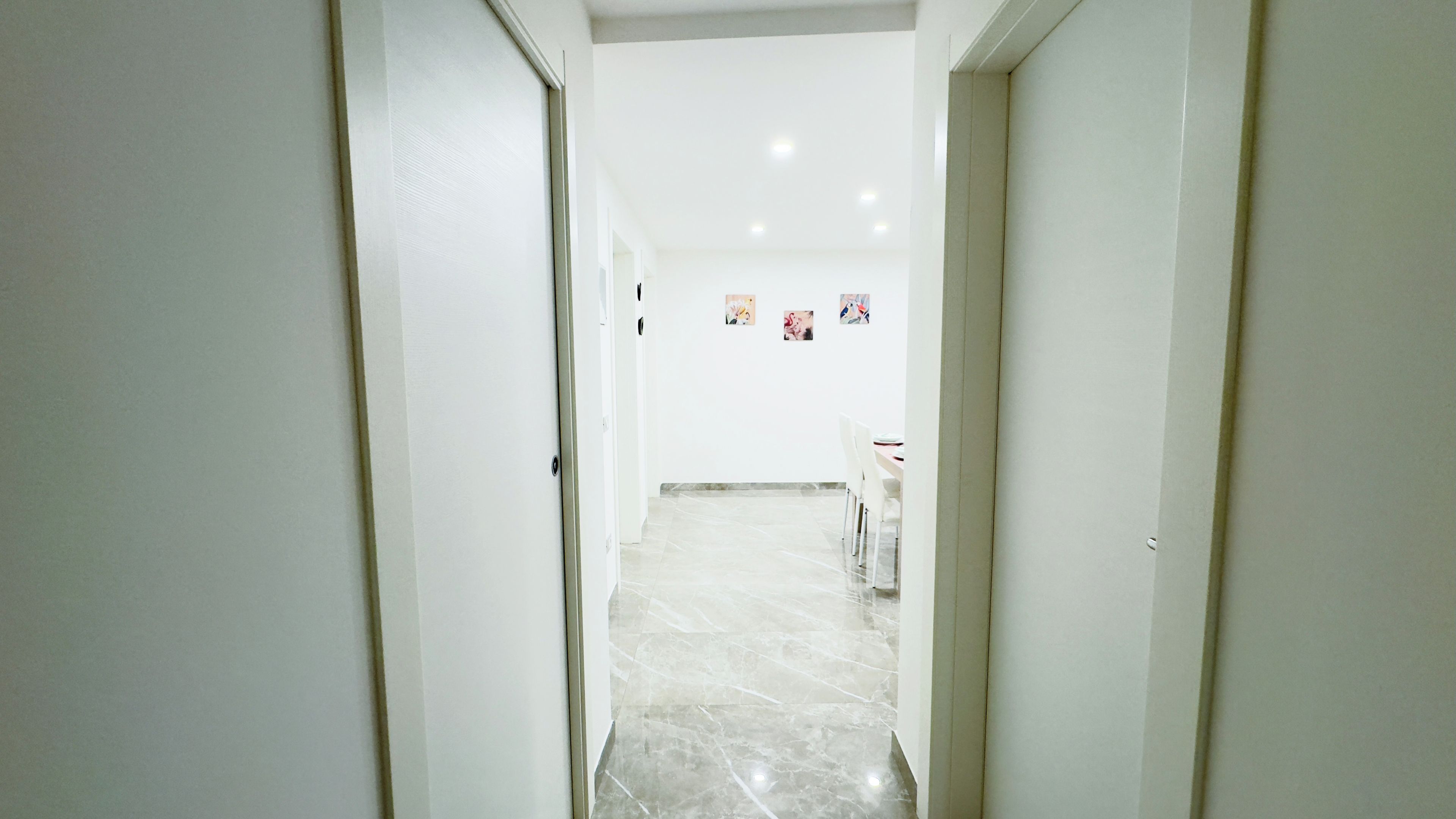 Un pasillo con paredes blancas y piso de mármol que conduce a una habitación con una mesa de comedor y sillas.