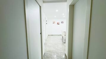 A hallway with white walls and a marble floor leading to a room with a dining table and chairs.