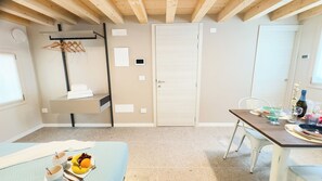 Una habitación con una cama, una mesa con una botella y vasos, un perchero y una puerta.
