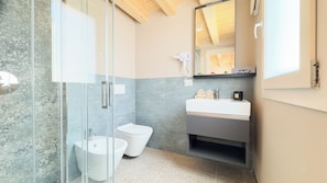 Un baño moderno con cabina de ducha de vidrio, un lavamanos blanco y un inodoro.