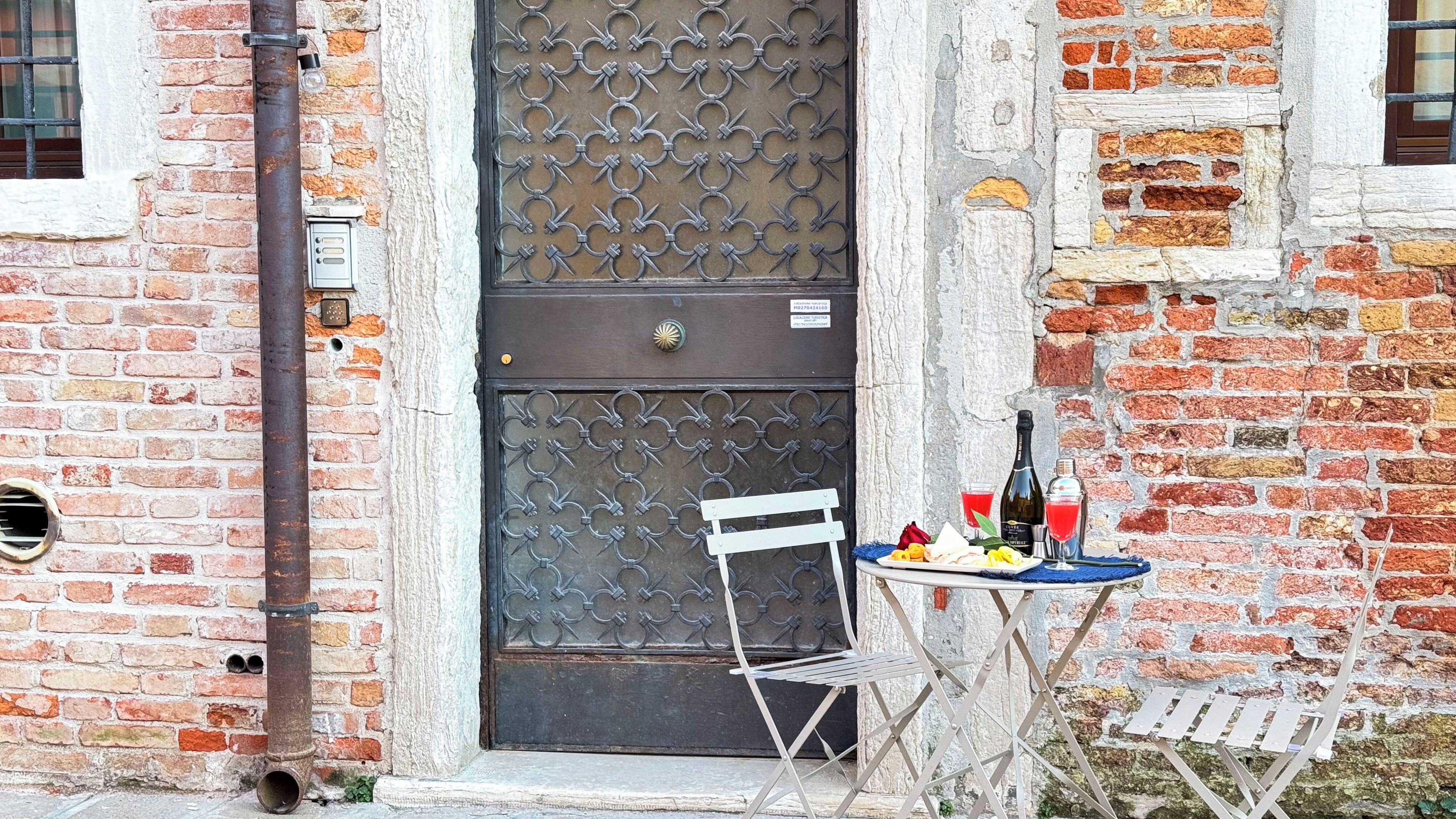 Un edificio rustico in mattoni con una porta metallica e un piccolo tavolo con una bottiglia e dei bicchieri.