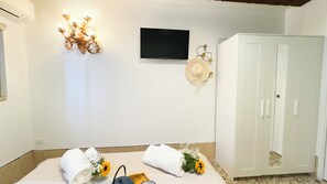 A room with a flat-screen TV mounted on the wall, a white wardrobe, and towels with flowers on the floor. - Gesuiti Cozy and Central Apartment by Ca-sa Check (Venice)