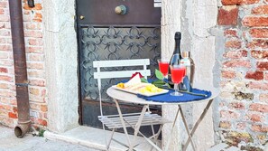 A small outdoor table with a white chair, a plate of food, two drinks, and a bottle of olive oil. - Gesuiti Cozy and Central Apartment by Ca-sa Check (Venice)