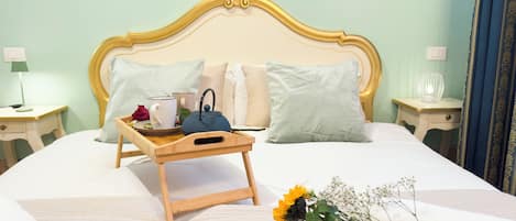 Un lit bien fait, sur lequel repose un plateau en bois contenant une théière, des tasses et une rose.