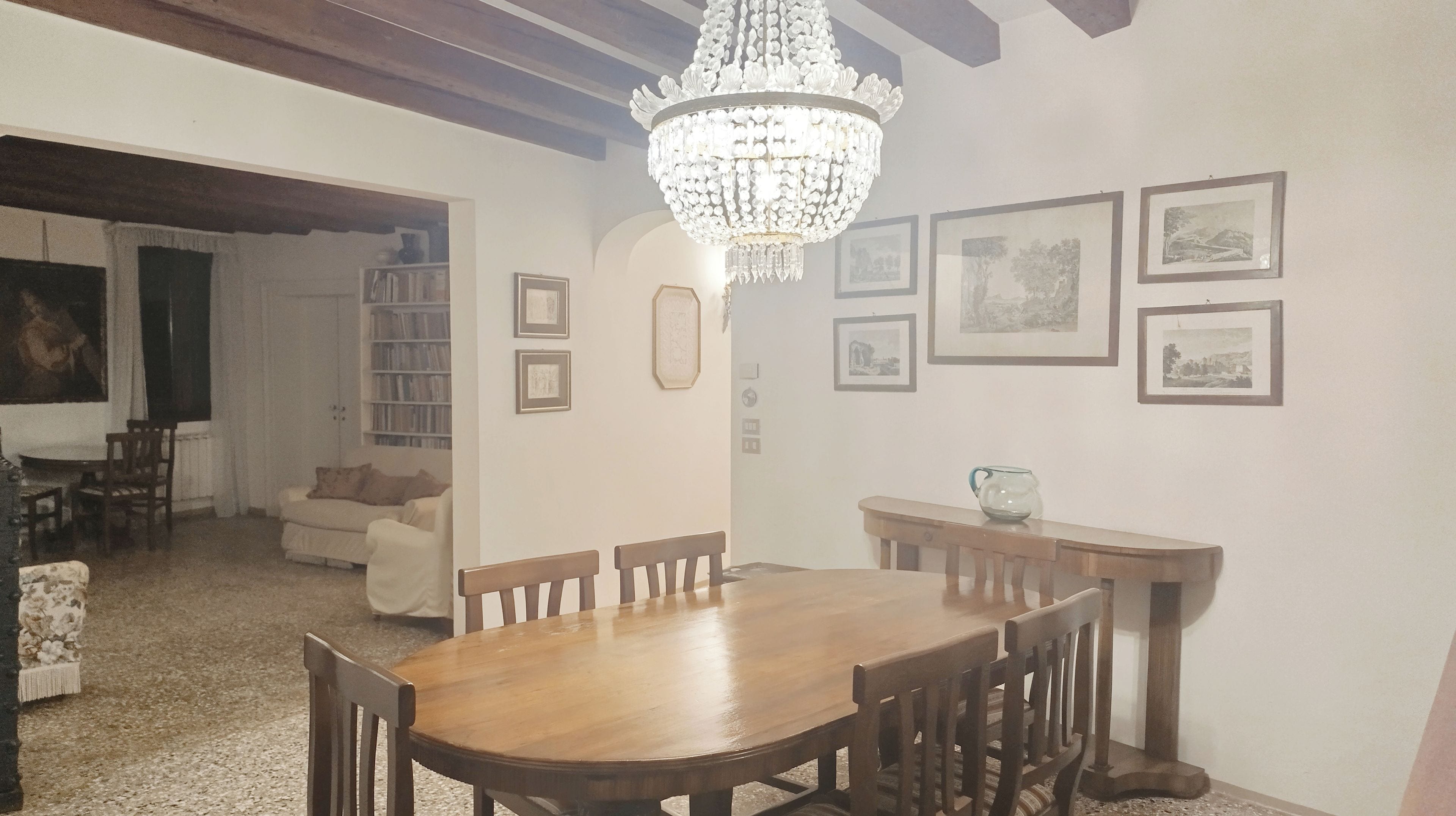 A dining area with a wooden table and chairs, a chandelier, and framed pictures on the wall.