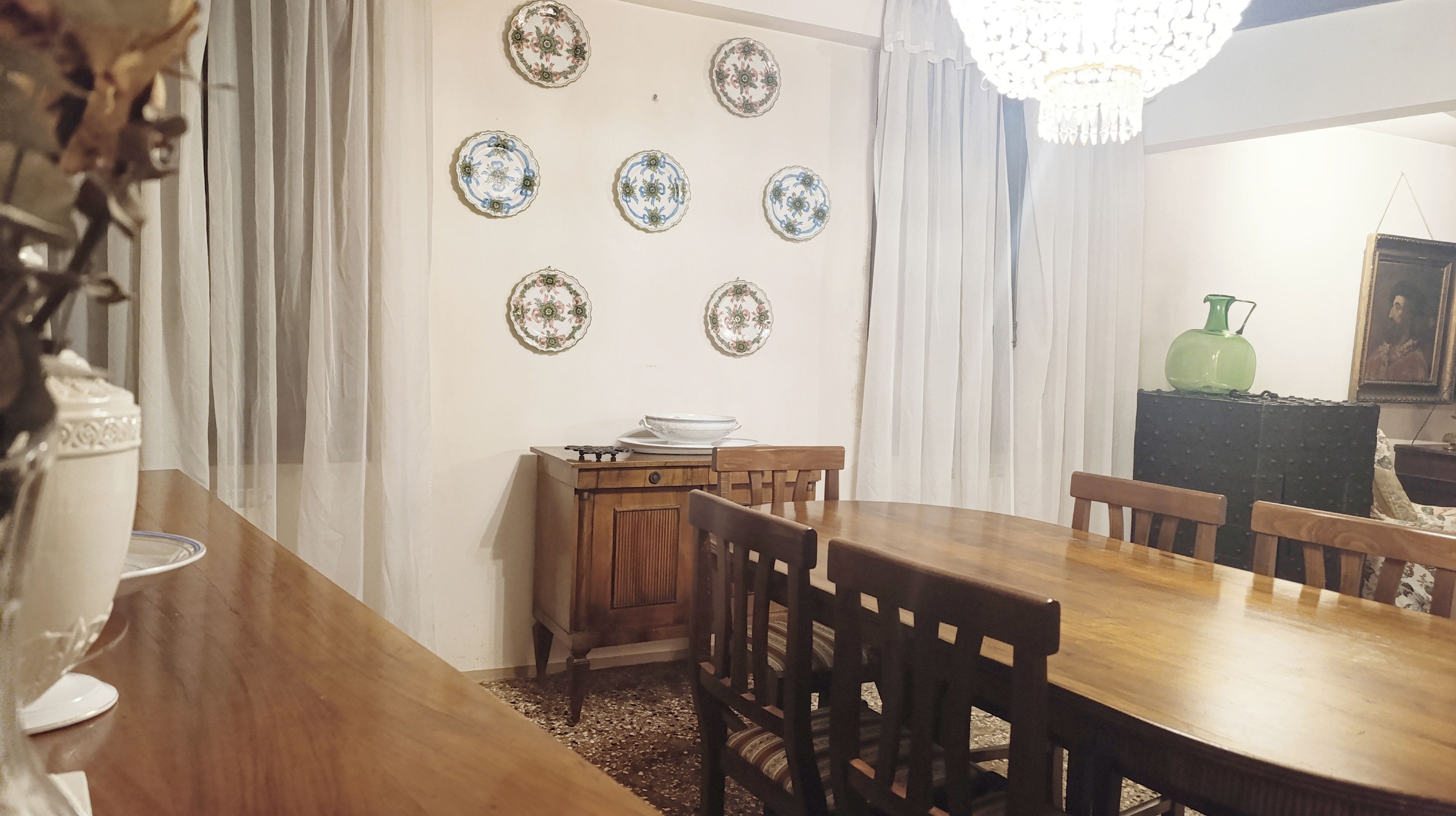 A dining area with a wooden table and chairs, a small cabinet, and decorative plates on the wall.