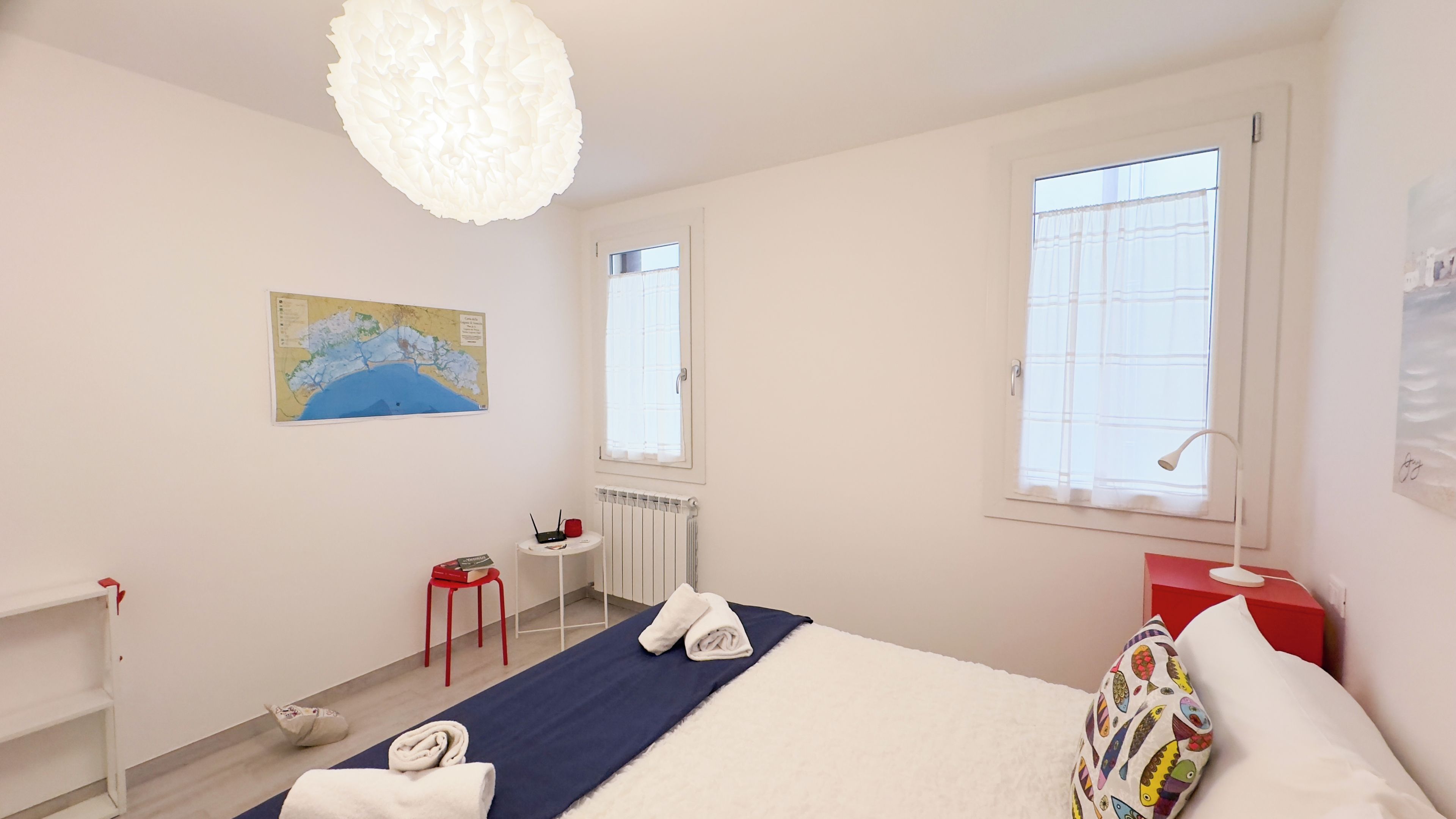Een slaapkamer met een bed, een kaart aan de muur, een bureau met een stoel en een raam.