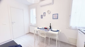 A small, clean room with a white door, a radiator, a table set with a bottle, glasses, and plates, and a clock on the wall. - Maison De La Brodeuse by Ca-sa Check (Chioggia)