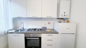 A compact kitchen with white cabinets, a gas stove, a built-in oven, a sink, and a Liebherr refrigerator. - Maison De La Brodeuse by Ca-sa Check (Chioggia)