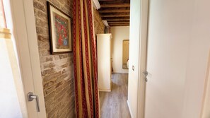 A hallway with a brick wall, a framed picture, a white door, and a red curtain. - Graceful Venice Barnaba Suite by Ca-sa Check (Venice)