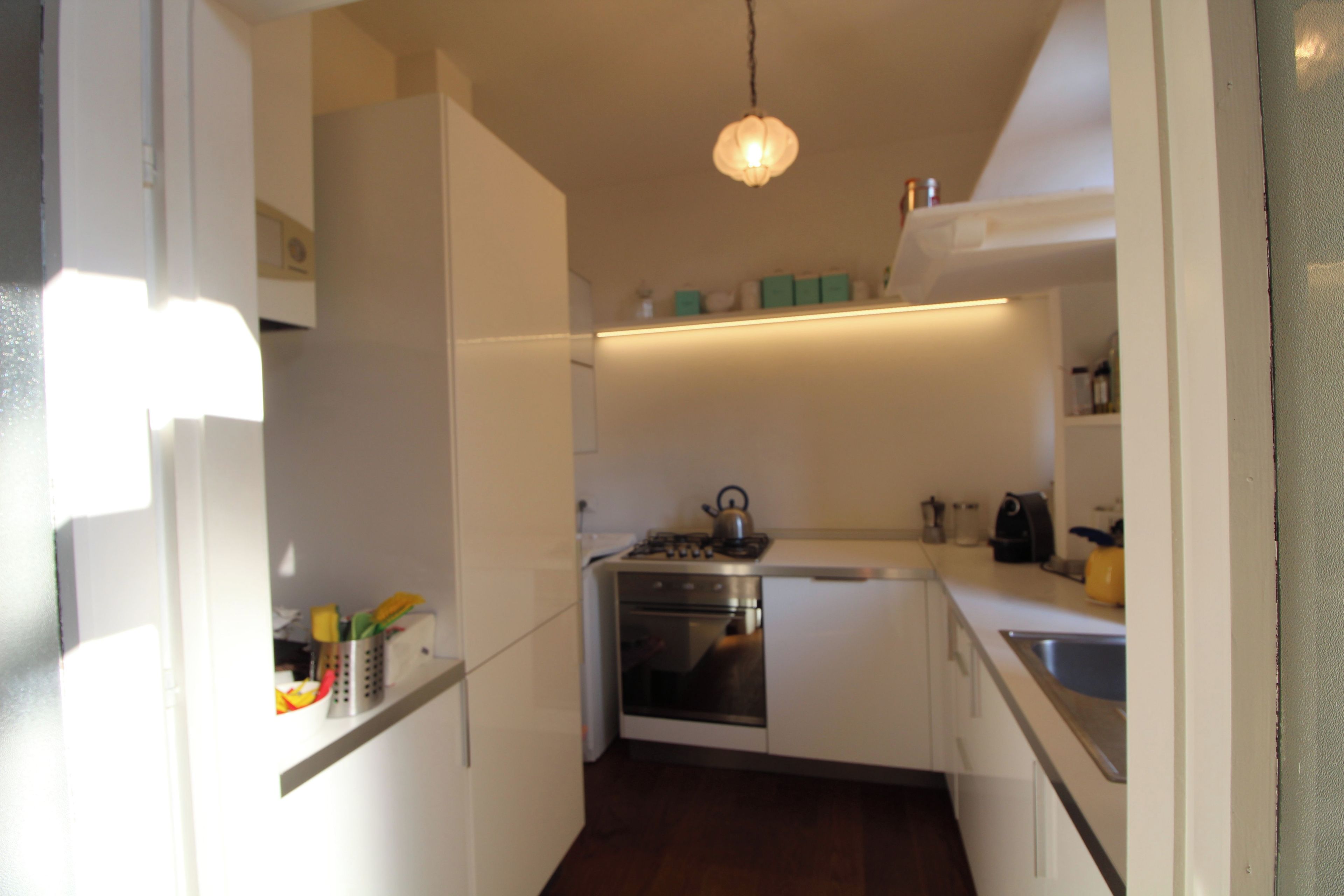 Een kleine keuken met witte kastjes, een kookplaat en een spoelbak.