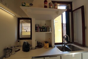 A kitchen with a coffee maker, a kettle, a sink, and various kitchen items on shelves. - Apartment in the Heart of Venice by Ca-sa Check (Venice)