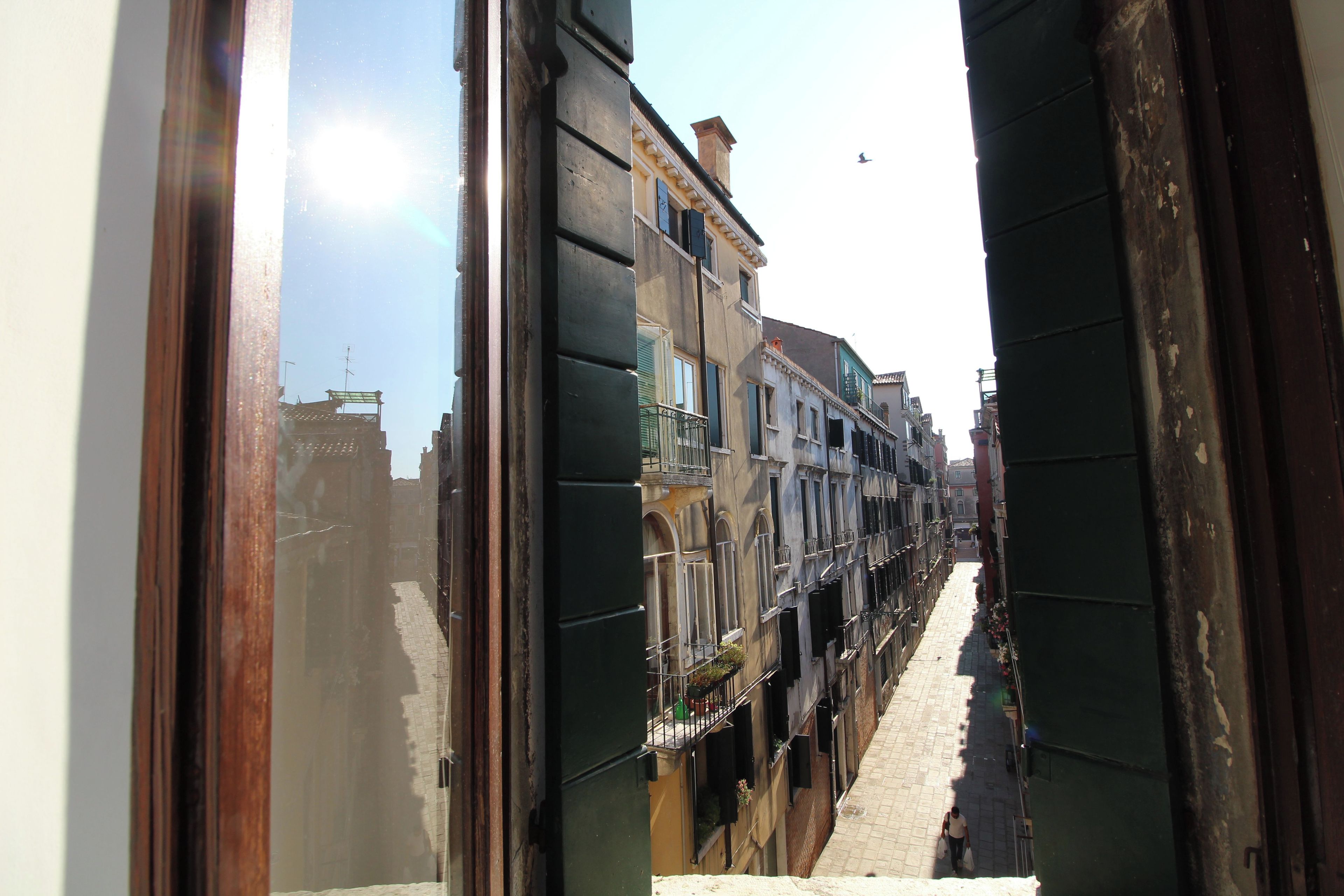 A narrow street with buildings on either side, a clear sky, and a person walking in the distance.