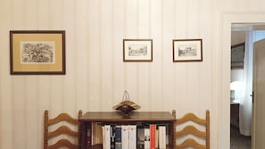 A room with striped wallpaper, a wooden chair, a small table with books, and three framed pictures on the wall. - Apartment Near Biennale Theatre by Ca-sa Check (Venice)