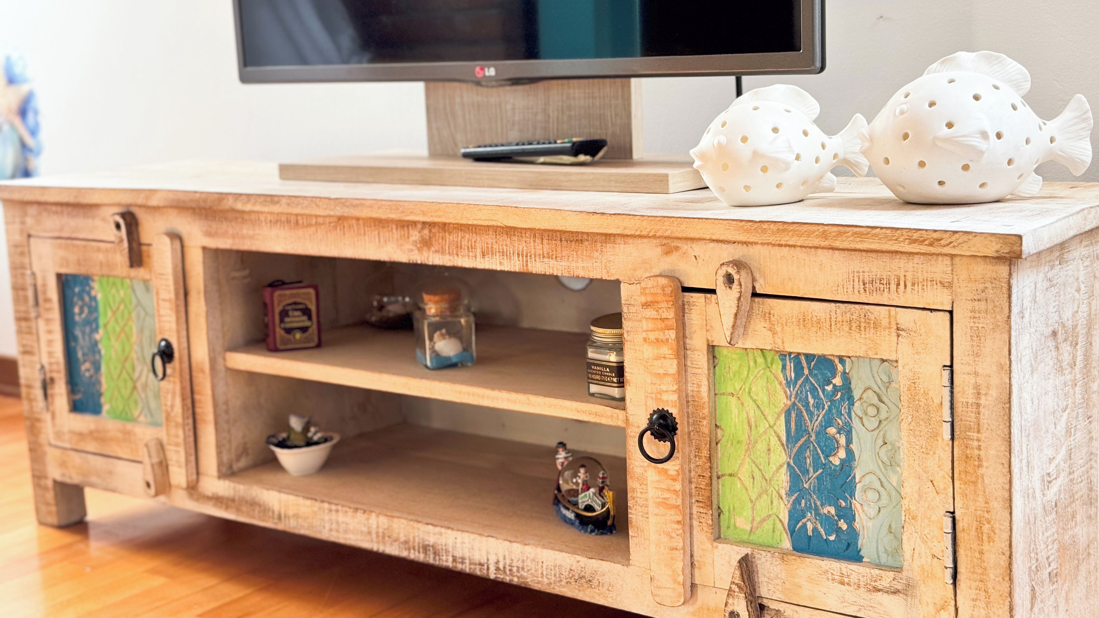 A wooden TV stand with a flat-screen TV on top, two decorative fish, and shelves with various items.