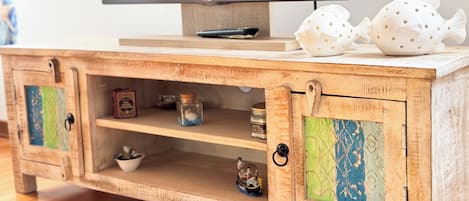 A wooden TV stand with a flat-screen TV on top, two decorative fish, and shelves with various items.