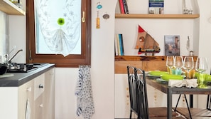 A kitchen with a window, a dining table with chairs, and a bookshelf with books and decorative items.