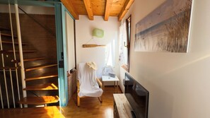 A staircase with wooden steps and a blue door frame leading to a room with a fireplace, a chair with a white cloth, and a wall-mounted painting.