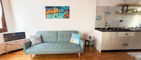 A living room with a grey sofa, a small table, and a painting of a cityscape.
