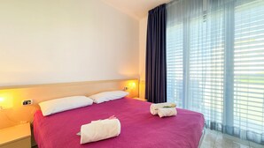 Ein Hotelzimmer mit einem großen Bett, zwei Kissen, einem Nachttisch mit Lampe und einem Fenster mit Jalousien.