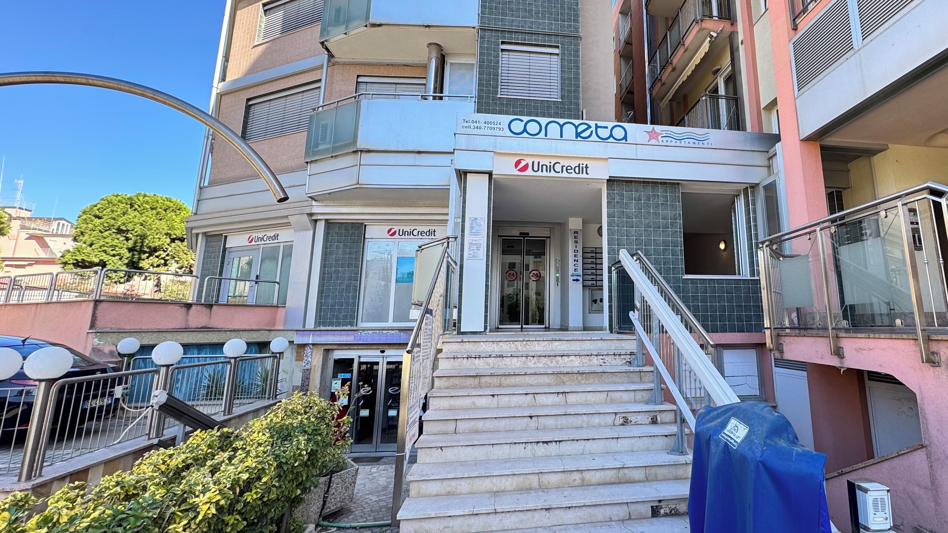 Um edifício com a placa 'cometa', a marca 'UniCredit' e uma escadaria que leva à entrada.