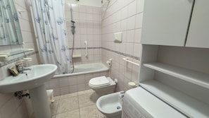 Een badkamer met een wastafel, toilet, hygiëneschuimer en bad.