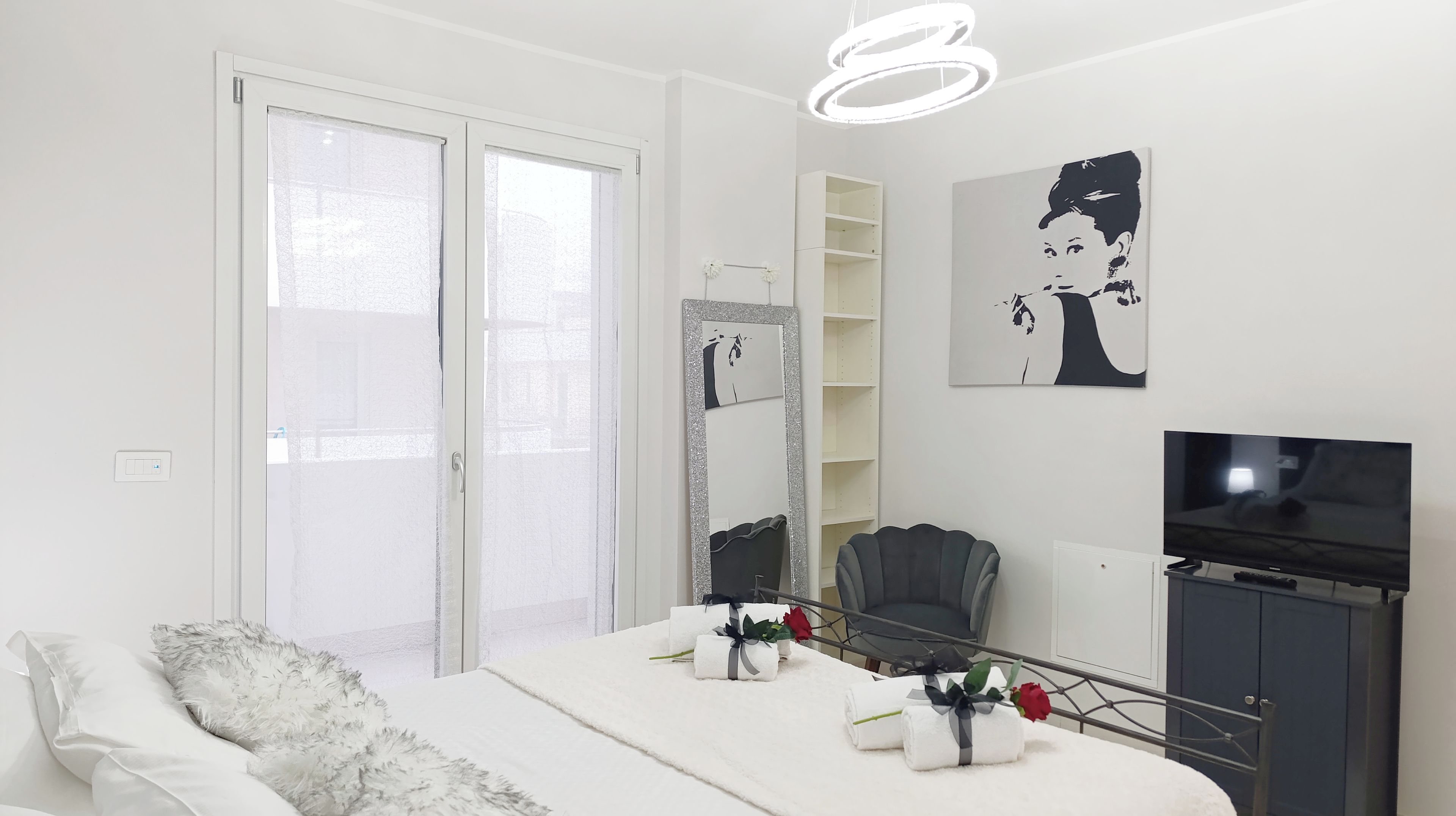 A modern bedroom with a bed, a chair, a TV, and a large mirror.