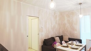 A dining area with a table set for four, a dark sofa with cushions, and a wall with a leaf pattern. - Casa Helios by Ca-sa Check (Chioggia)