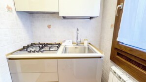 Una cocina compacta con estufa a gas, pileta de acero inoxidable y alacenas blancas.