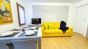 Una sala de estar moderna con un sofá amarillo, un televisor de pantalla plana y un comedor con una mesa dispuesta para dos personas.